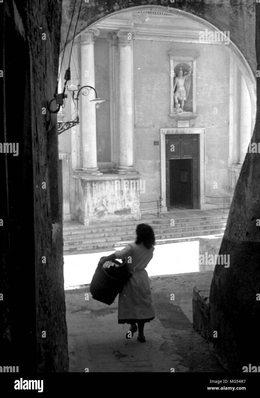 Eine junge italienische Frau trägt einen Korb durch die verlassenen Straßen von Rom, Italien, in den 1930er Jahren, vielleicht auf dem Weg zum Markt. Stockfoto