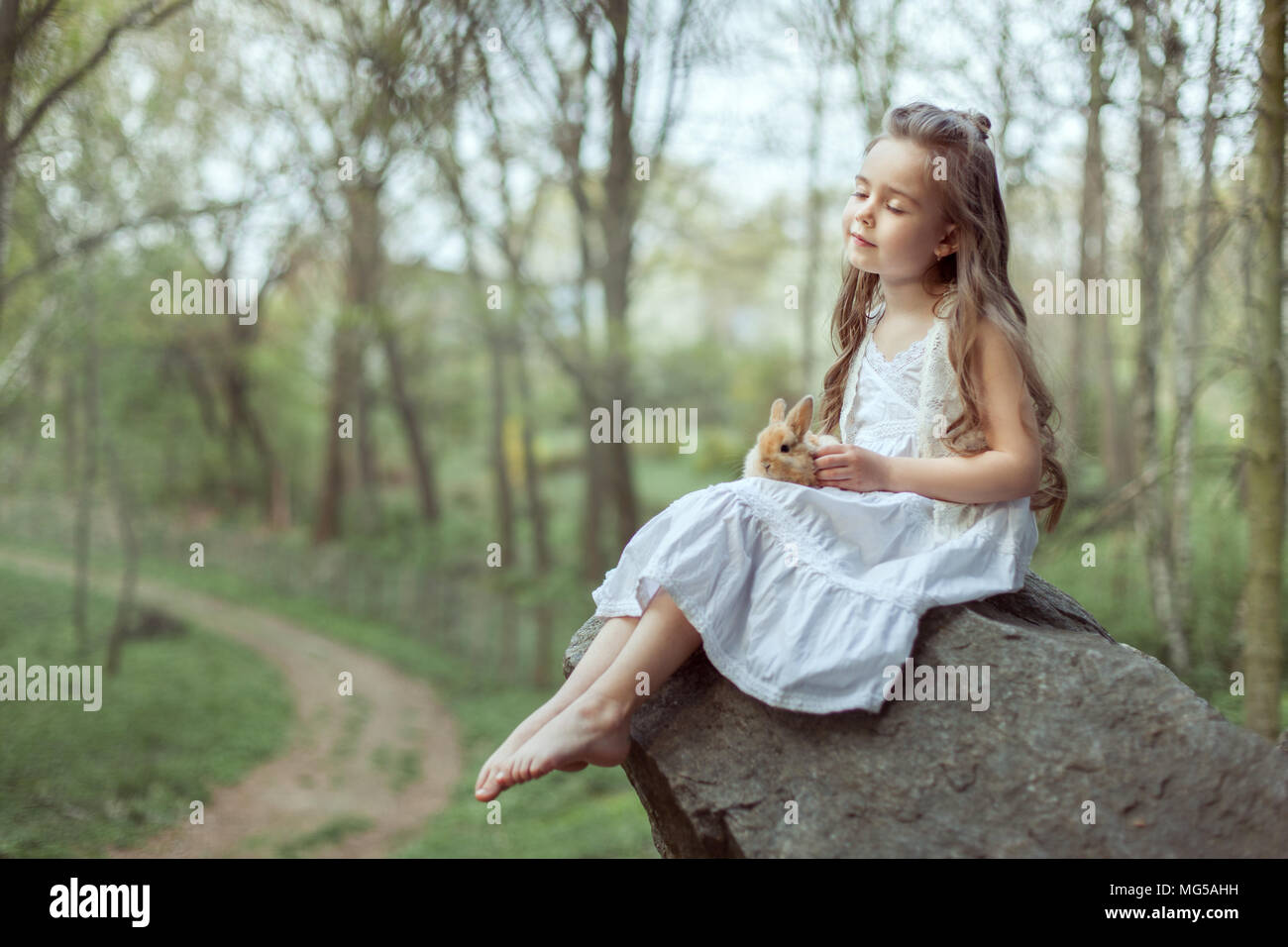 Kleines Mädchen sitzt auf einer Klippe. Sie schloss die Augen und hielt eine kleine Kaninchen in ihren Händen. Stockfoto