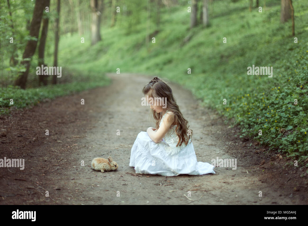 Kleines Mädchen sitzen auf der Straße in den Wald. Vor ihr sitzt ein kleiner Hase. Stockfoto