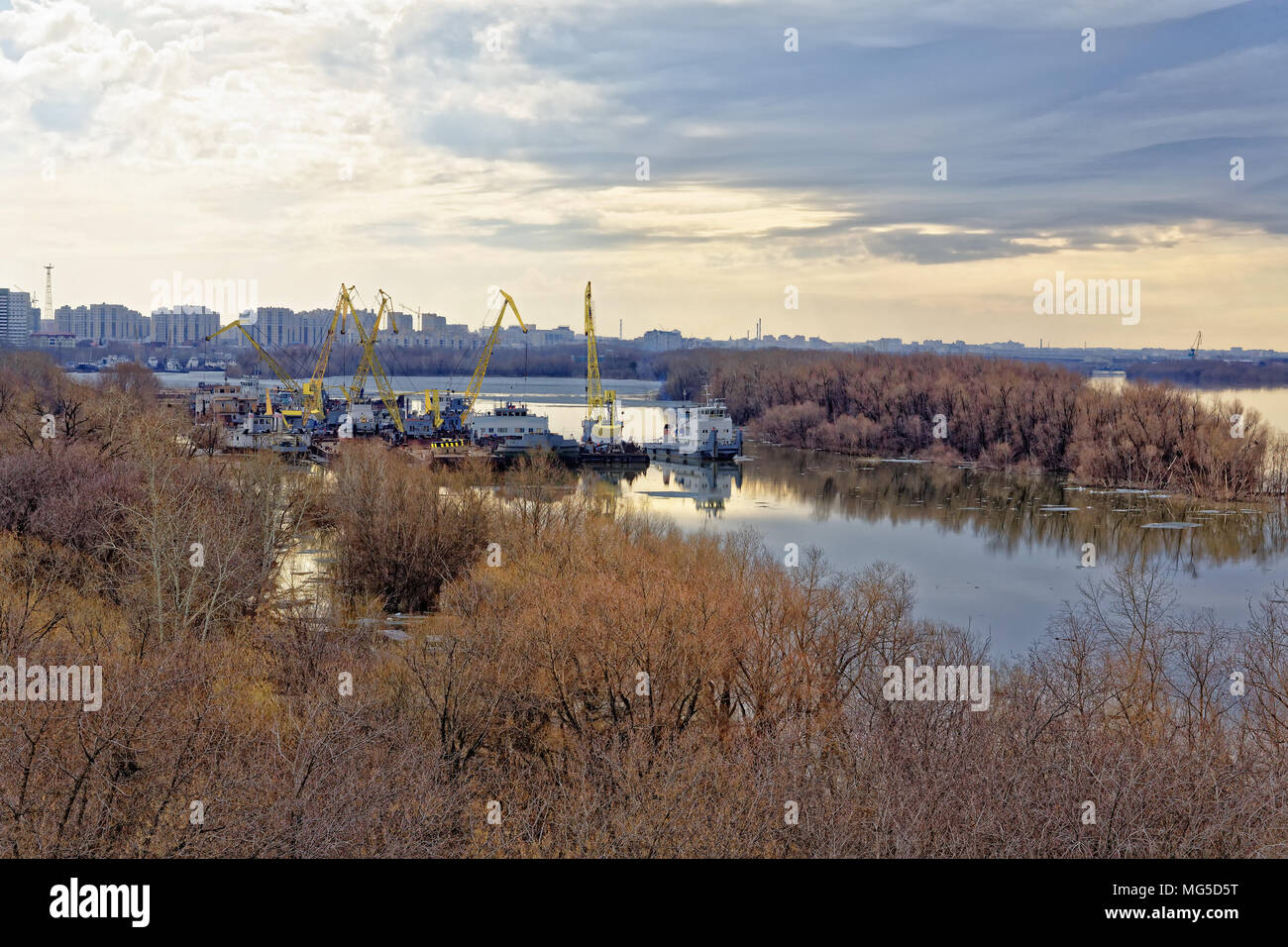 Russland, Omsk. Schlepper, Schwimmkrane und Schiffe in einem provinznest auf dem irtysch Fluss geparkt. Im Hintergrund, Silhouetten von modernen Wohngebäuden mult Stockfoto