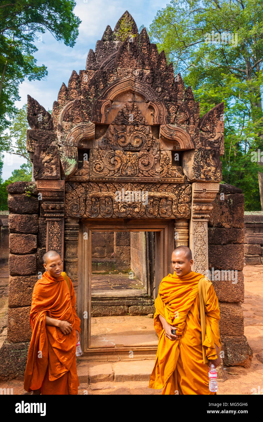 Zwei Buddhistische Mönche, in einem gelben und orangefarbenen Robe, stehen vor der Tür, eine Galerie in der zweiten Gehäuse der Kambodschanischen Banteay Srei. Stockfoto