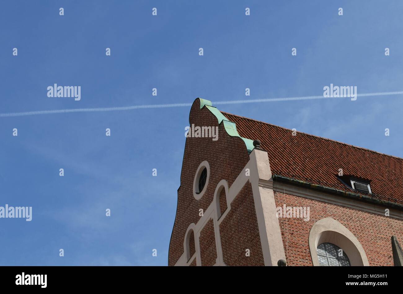 Historisches Gebäude mit roten Ziegeln und ein kondensstreifen eines Flugzeugs in den blauen Himmel geschossen in München in Deutschland Stockfoto