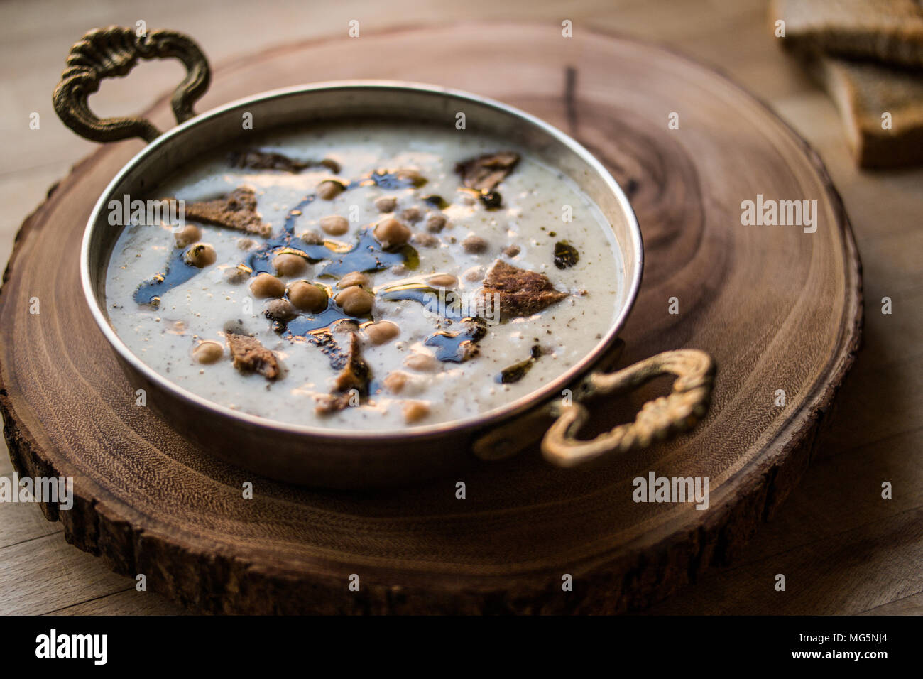 Türkische Yuvalama Suppe mit Joghurt und Kichererbsen in einer Kupfer Schale auf einem hölzernen Oberfläche. Stockfoto