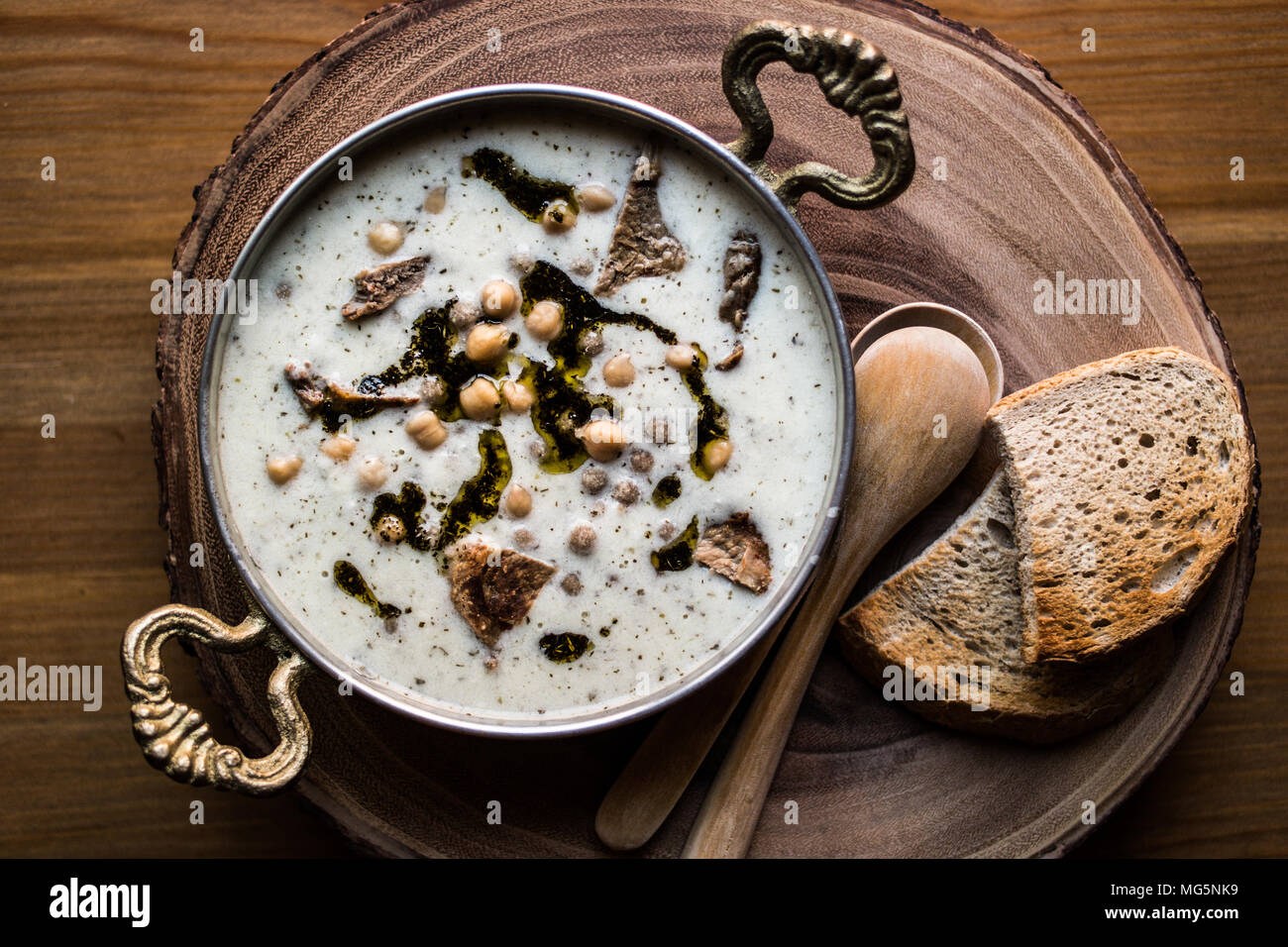Türkische Yuvalama Suppe mit Joghurt und Kichererbsen in einer Kupfer Schale auf einem hölzernen Oberfläche. Stockfoto