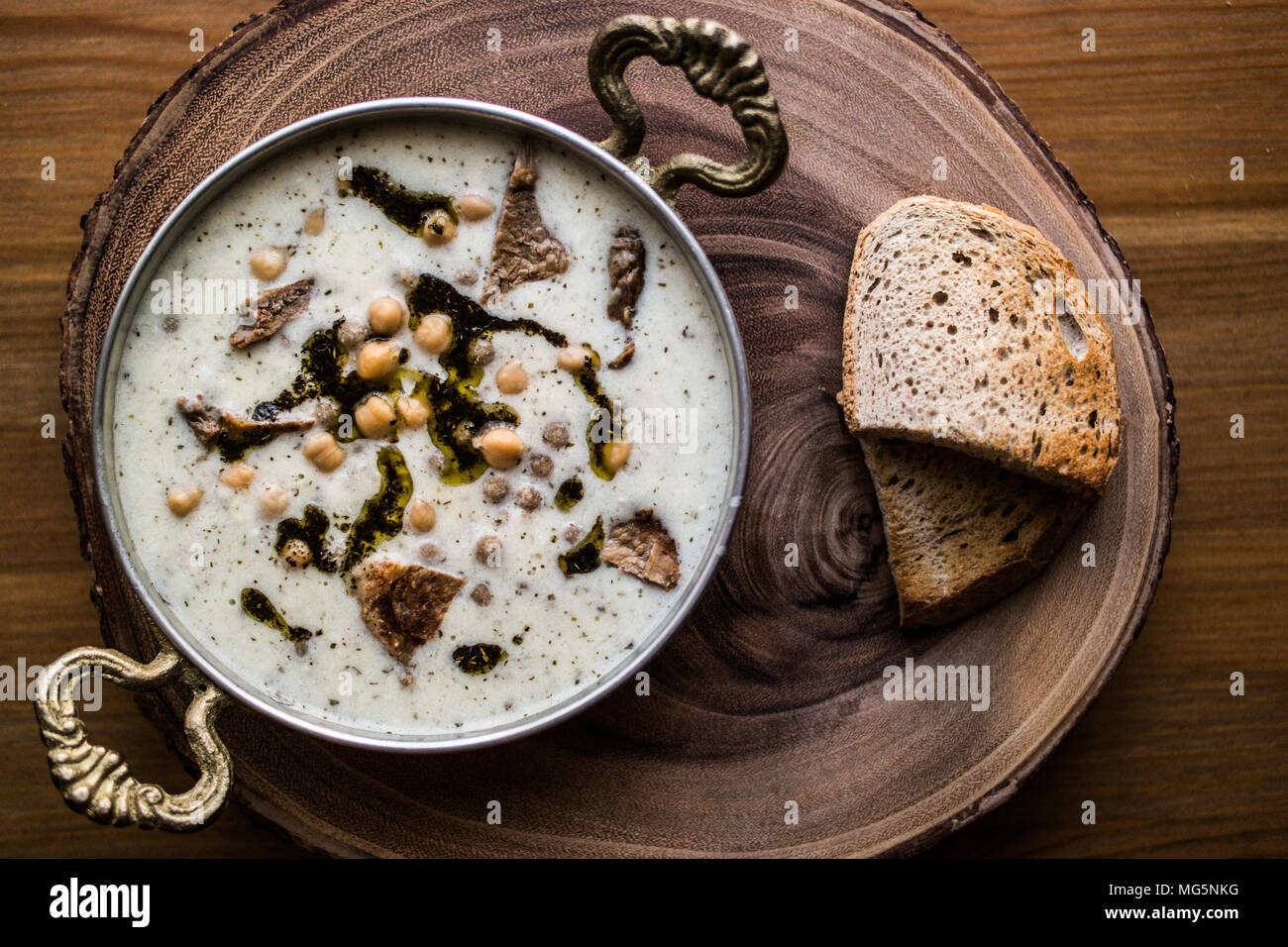 Türkische Yuvalama Suppe mit Joghurt und Kichererbsen in einer Kupfer Schale auf einem hölzernen Oberfläche. Stockfoto