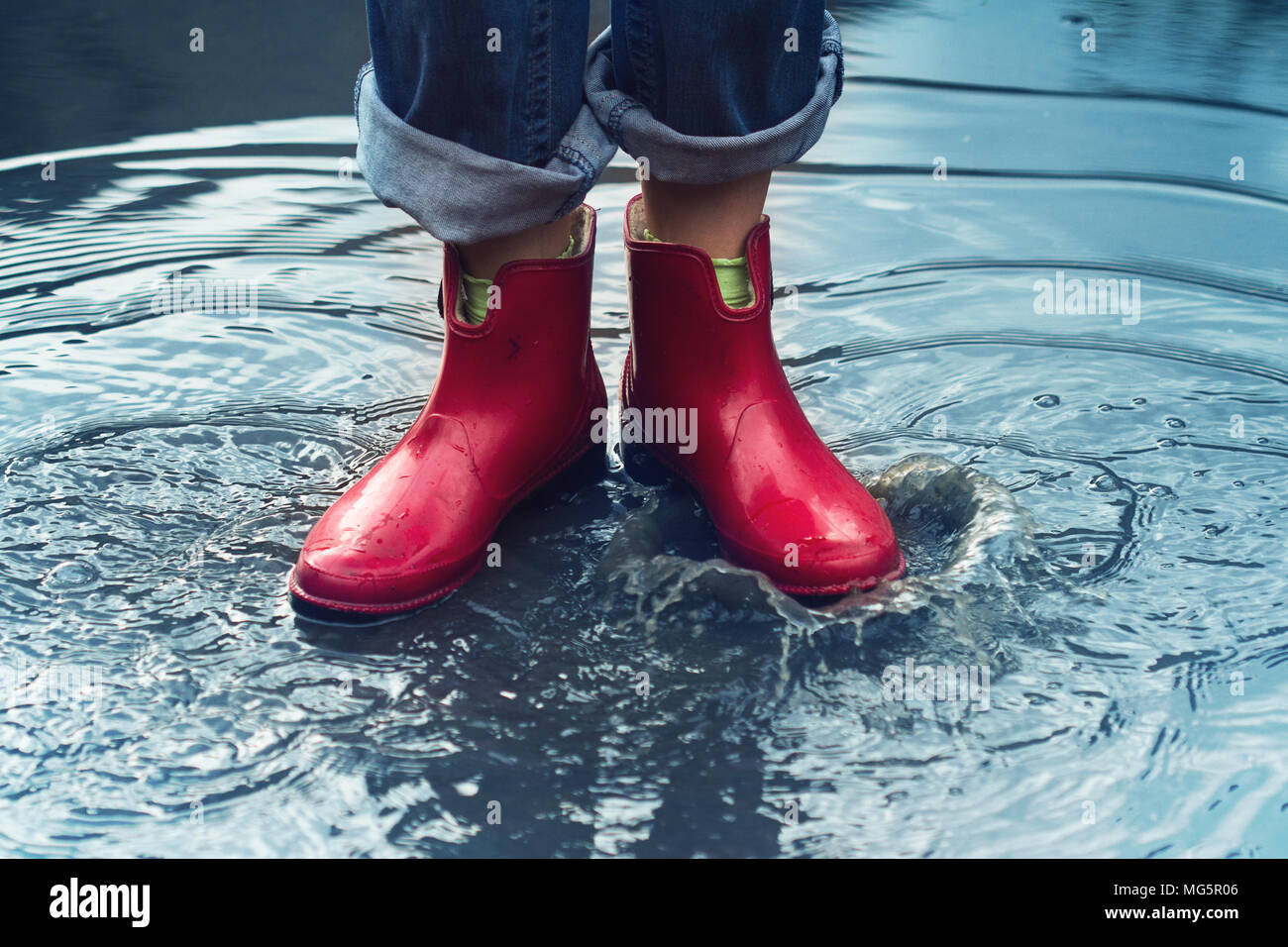 Vorderansicht Nahaufnahme des jungen kaukasischen Frau Füße mit Rot kurze Stiefel und Jeans in einer Pfütze von Wasser nach dem Regen auf einer Straße der Stadt Stockfoto