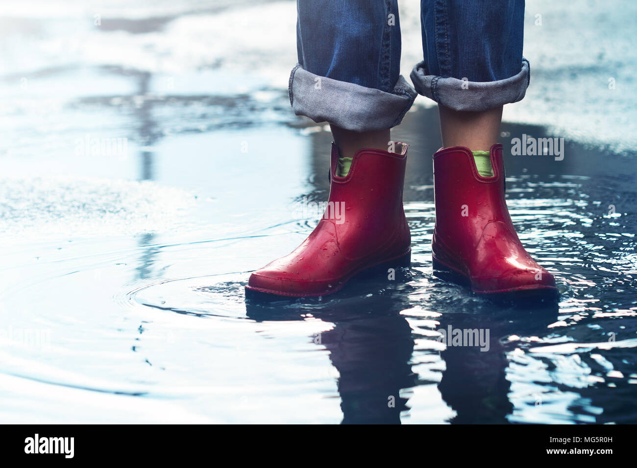 Vorderansicht Nahaufnahme des jungen kaukasischen Frau Füße mit Rot kurze Stiefel und Jeans in einer Pfütze von Wasser nach dem Regen auf einer Straße der Stadt Stockfoto