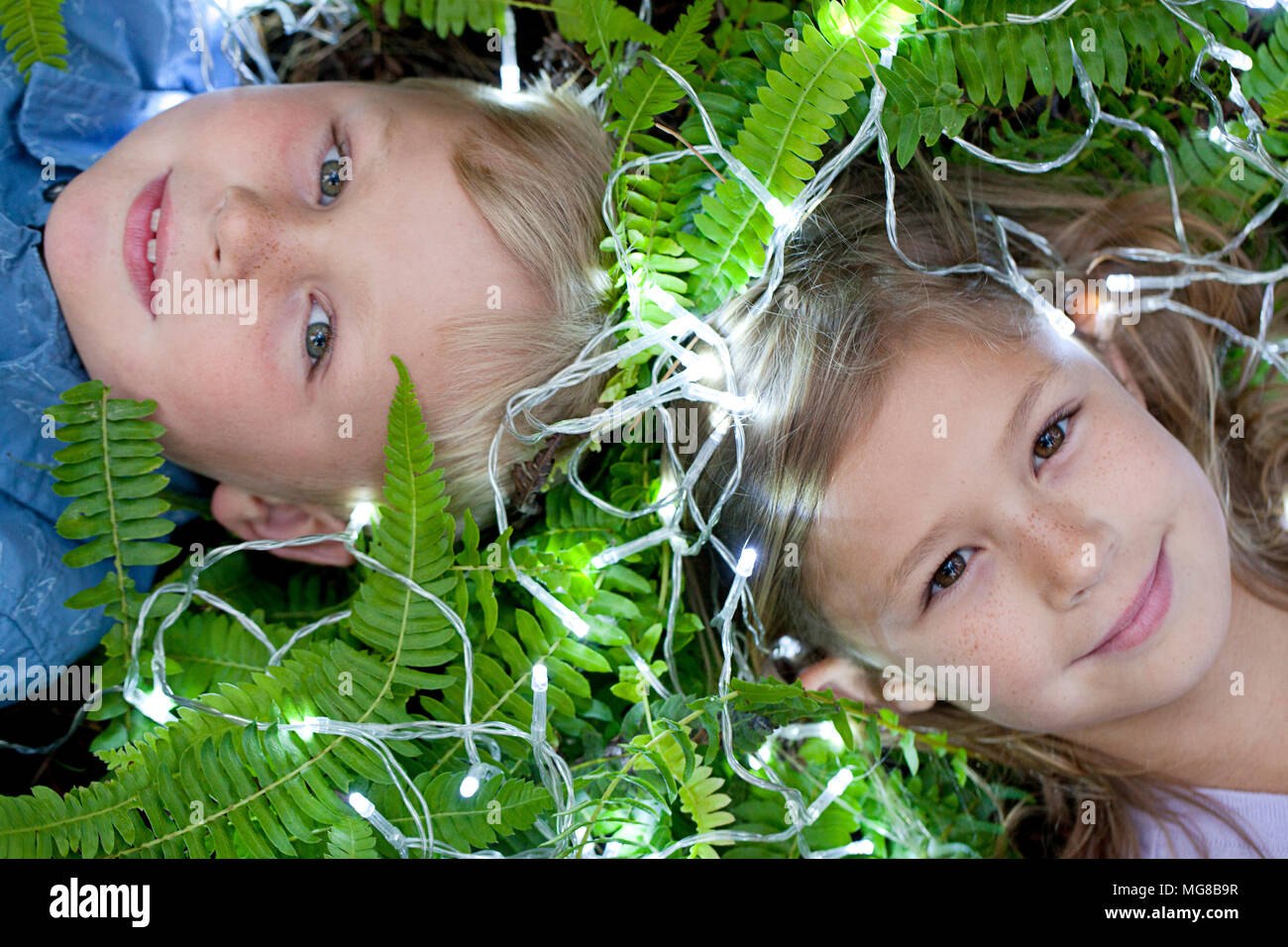 Zwei Kinder unter Farnblätter mit Lichterketten Stockfoto