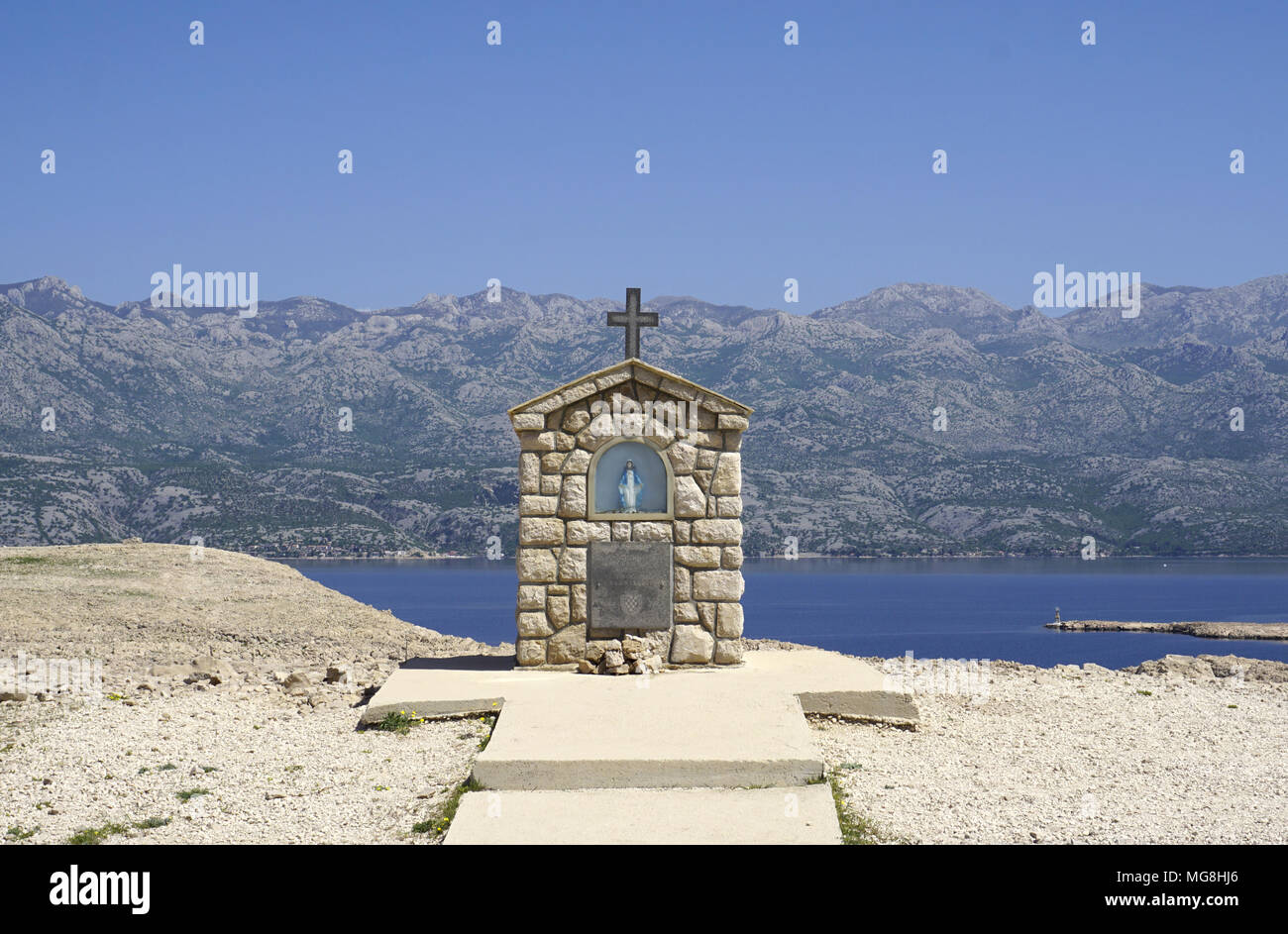 Kleine Kapelle mit Maria Statue auf der Insel Pag Dalmatien, mit dem Velebit Gebirge im Hintergrund in Kroatien Stockfoto