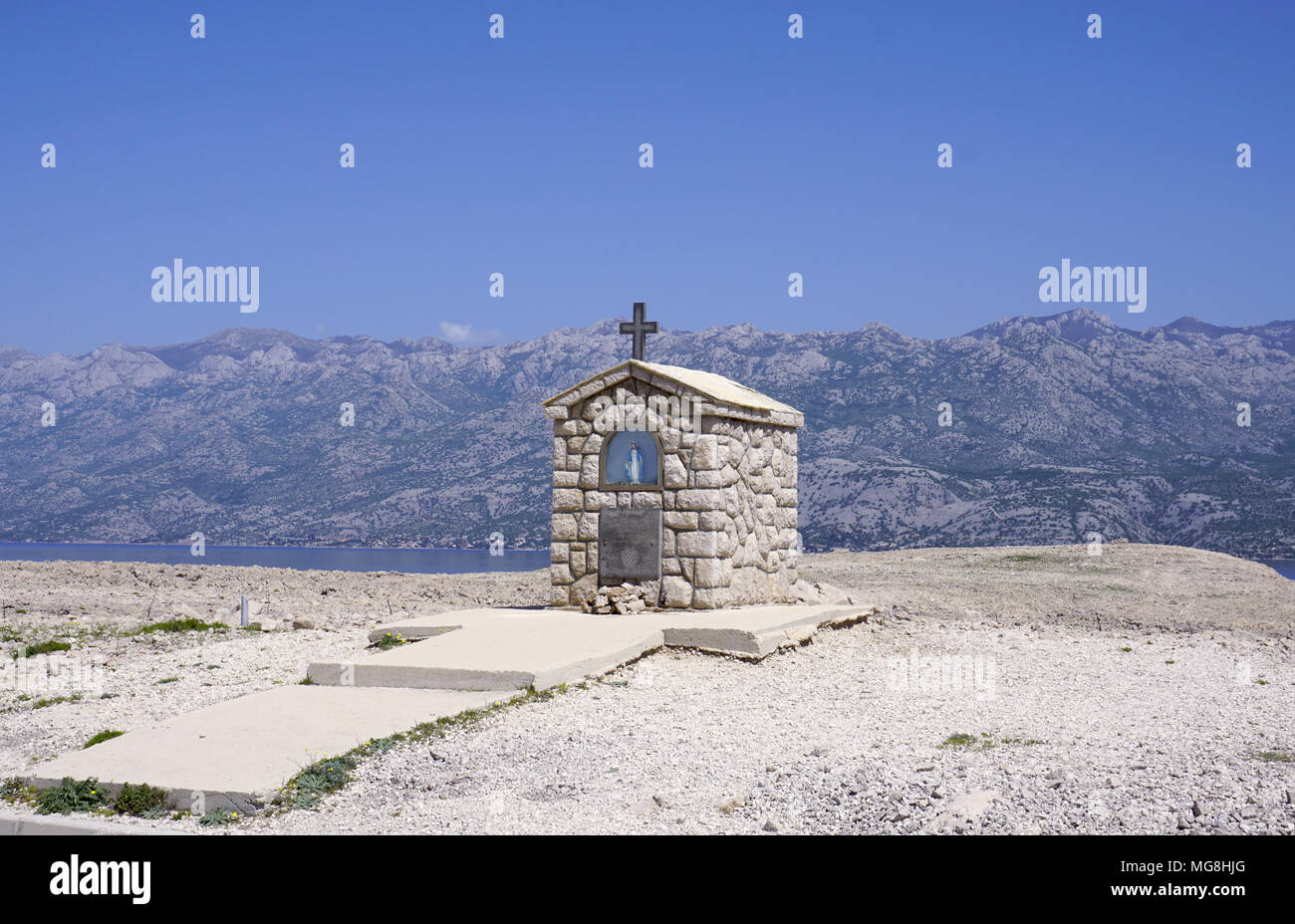 Kleine steinerne Kapelle mit Maria Statue vor der Berg Velebit, am Rande der Insel Pag in Kroatien Stockfoto