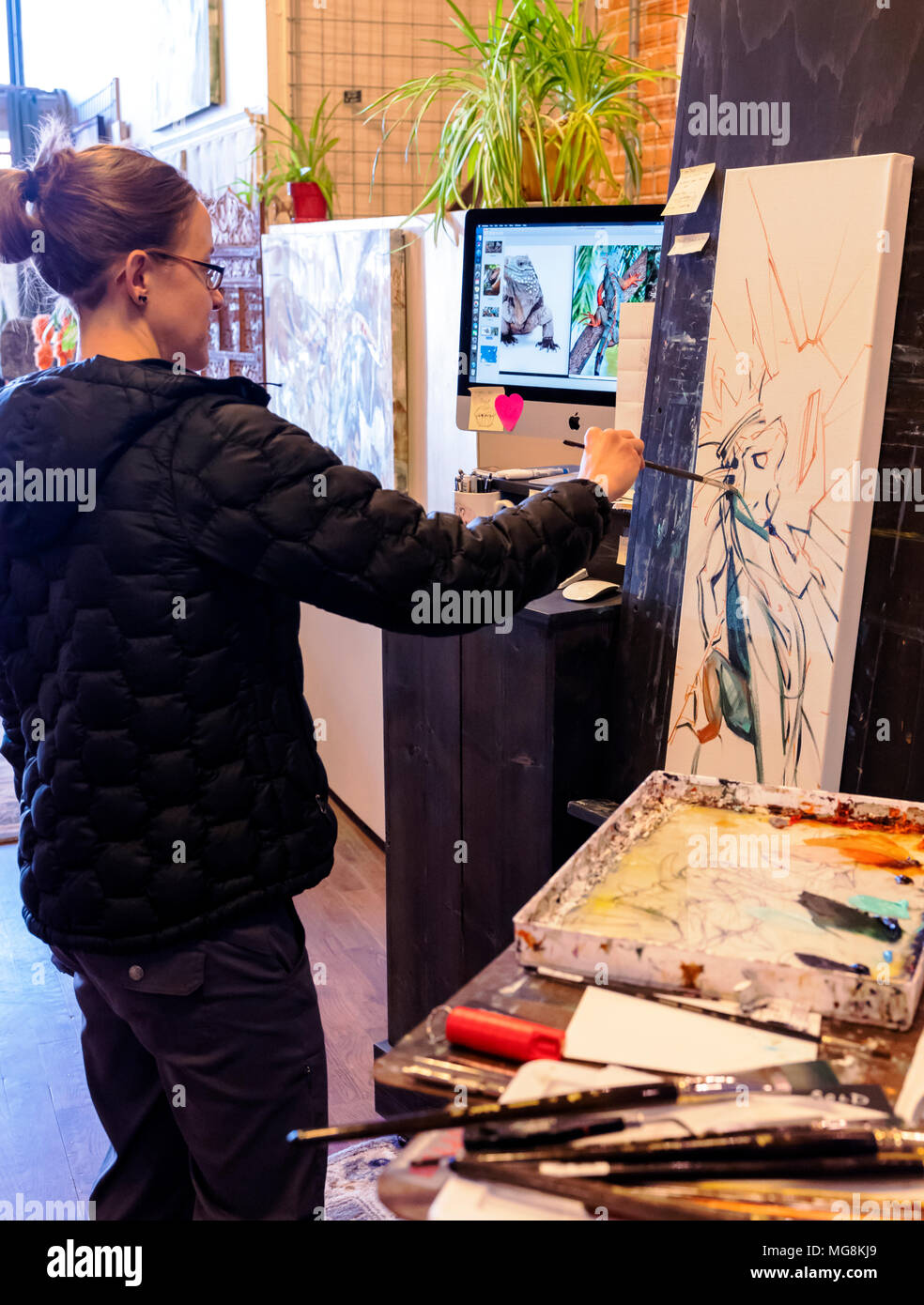 Bildende Künstlerin Katie Maher referenzieren Computer ein Bild beim Erstellen ein Ölgemälde in Ihrer Galerie; Salida, Colorado, USA Stockfoto