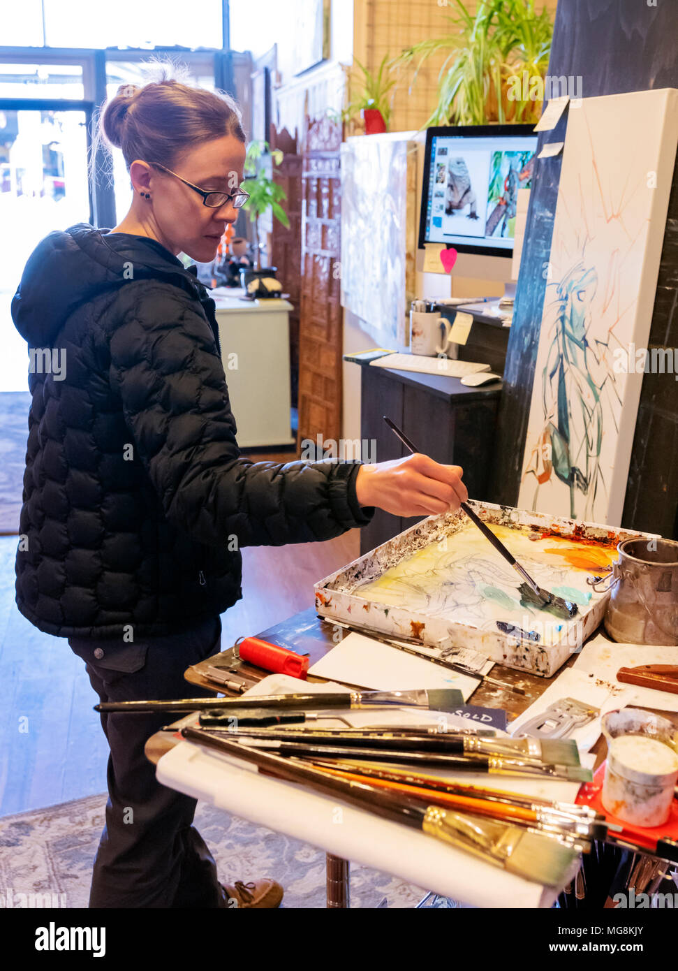 Bildende Künstlerin Katie Maher referenzieren Computer ein Bild beim Erstellen ein Ölgemälde in Ihrer Galerie; Salida, Colorado, USA Stockfoto