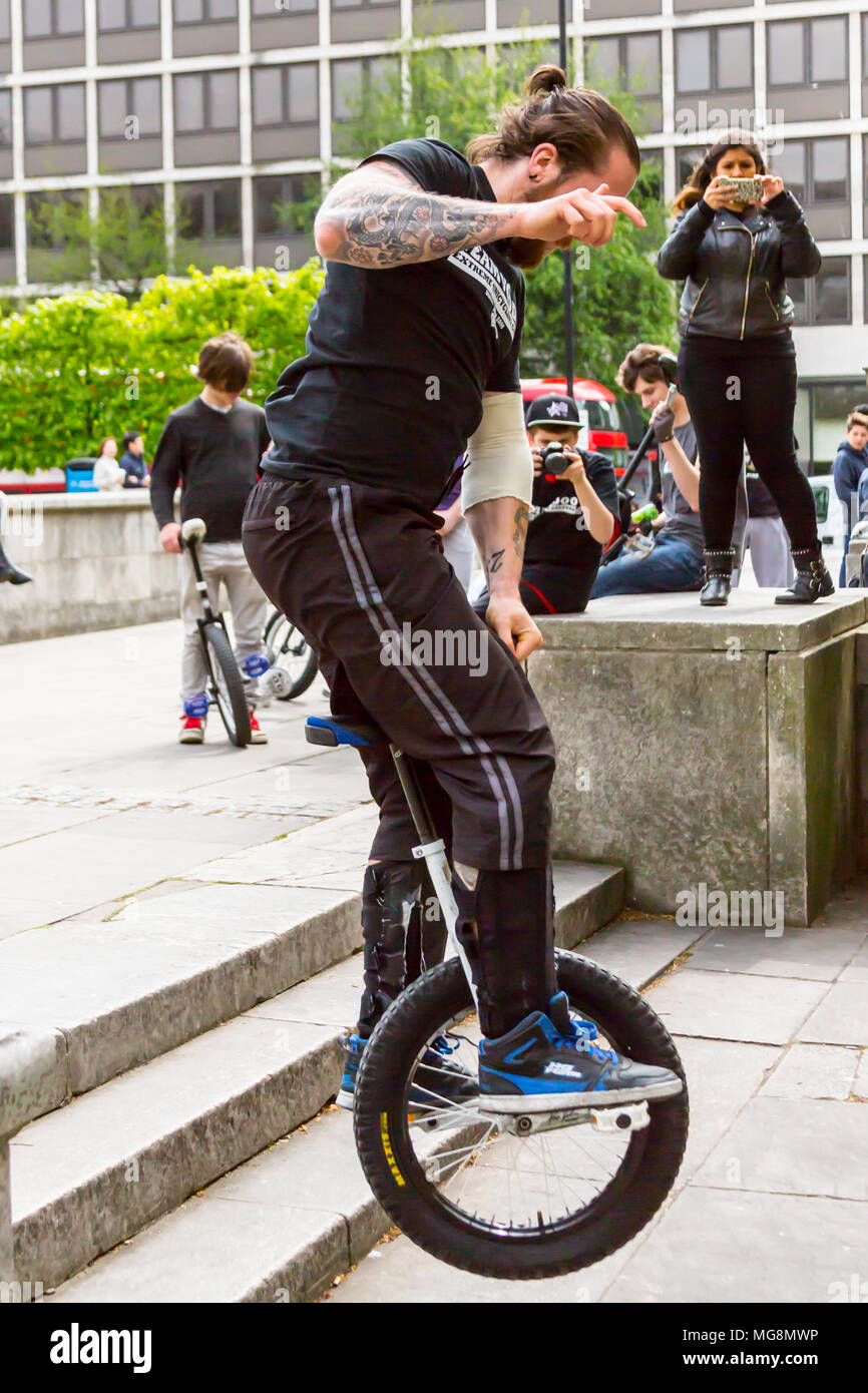 London, Großbritannien - 2. Mai 2015: Ein junger Mann mit Tätowierungen reitet ein ein Rad (mono) aus einer Reihe von Schritten, während Freunde Fotos zu machen. Stockfoto