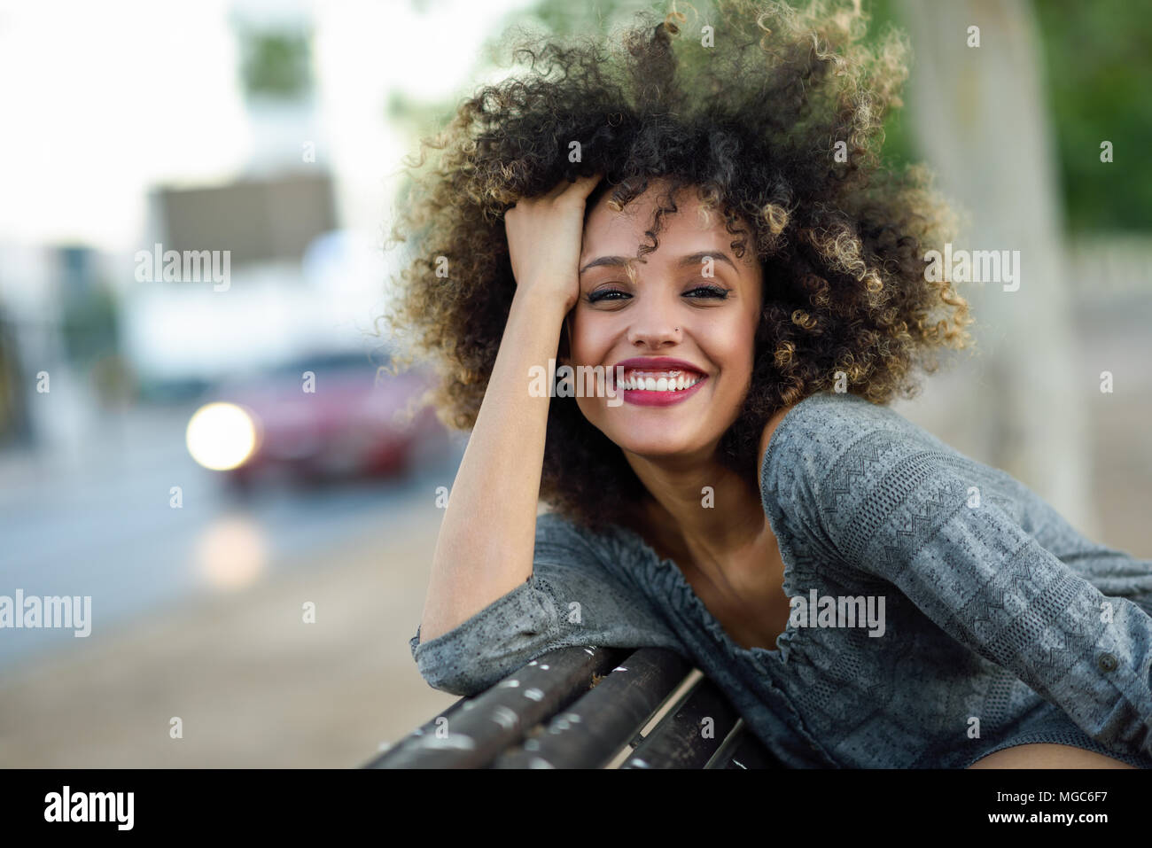 Junge gemischte Frau mit Afro Frisur lächelnd im städtischen Hintergrund. Schwarze Mädchen legere Kleidung. Stockfoto