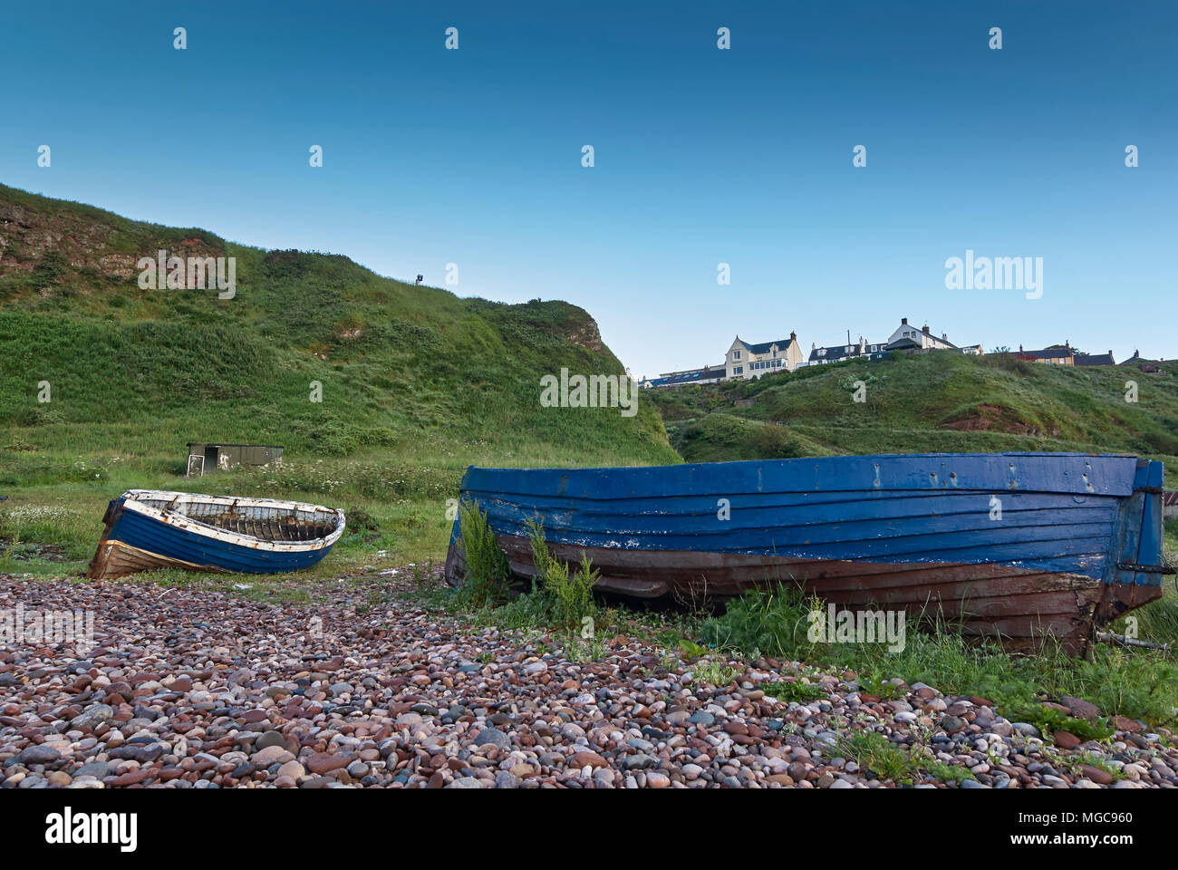 Ein paar der alten, verlassenen offene hölzerne Fischerboote liegen am Strand unterhalb der Klippen Dorf Auchmithie, in der Nähe von Arbroath, in Angus, Schottland. Stockfoto