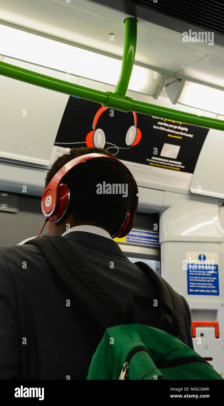 Menschen, die auf der Londoner U-Bahn, das Tragen der roten Kopfhörer, stehen unter einem Plakat werbung red Kopfhörer, Rückansicht Stockfoto