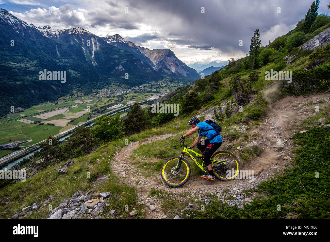 Ein Mann reitet ein Mountainbike hoch über dem Talboden in der Nähe der Städte Gampel und Jeizinen im Wallis Fläche der Schweiz. Stockfoto