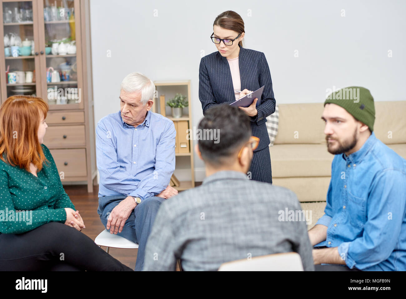 Gruppe von Patienten, die die Ausbildung ihrer sozialen Fähigkeiten, während im Kreis sitzen und die Teilnahme an Therapiesitzung, hoch professionellen Psychologen halten Stockfoto