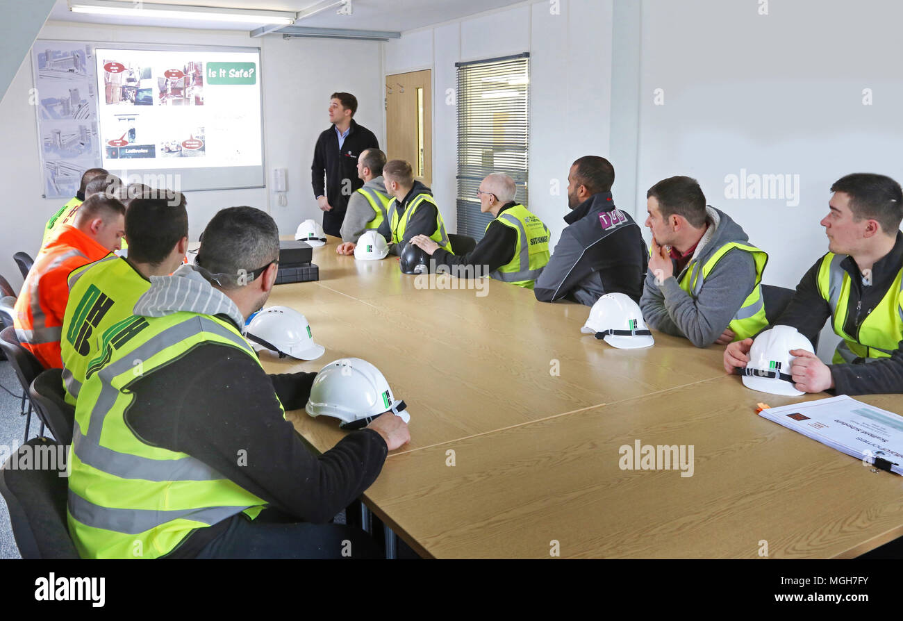 Im Londoner Baustellenbüro findet eine Gesundheits- und Sicherheitsunterweisung für Baustellen statt. Bauarbeiter nehmen mit ihren Schutzhelmen auf dem Tisch zu. Stockfoto
