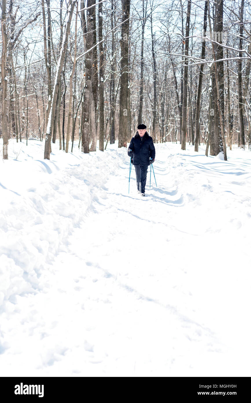 UFA, Russland, 29. MÄRZ 2018 - Ältere Menschen im Winter Kleidung geht mit Nordic Walking Stöcke durch einen Waldweg in schneefall Einsatz der Stöcke zu im Stockfoto