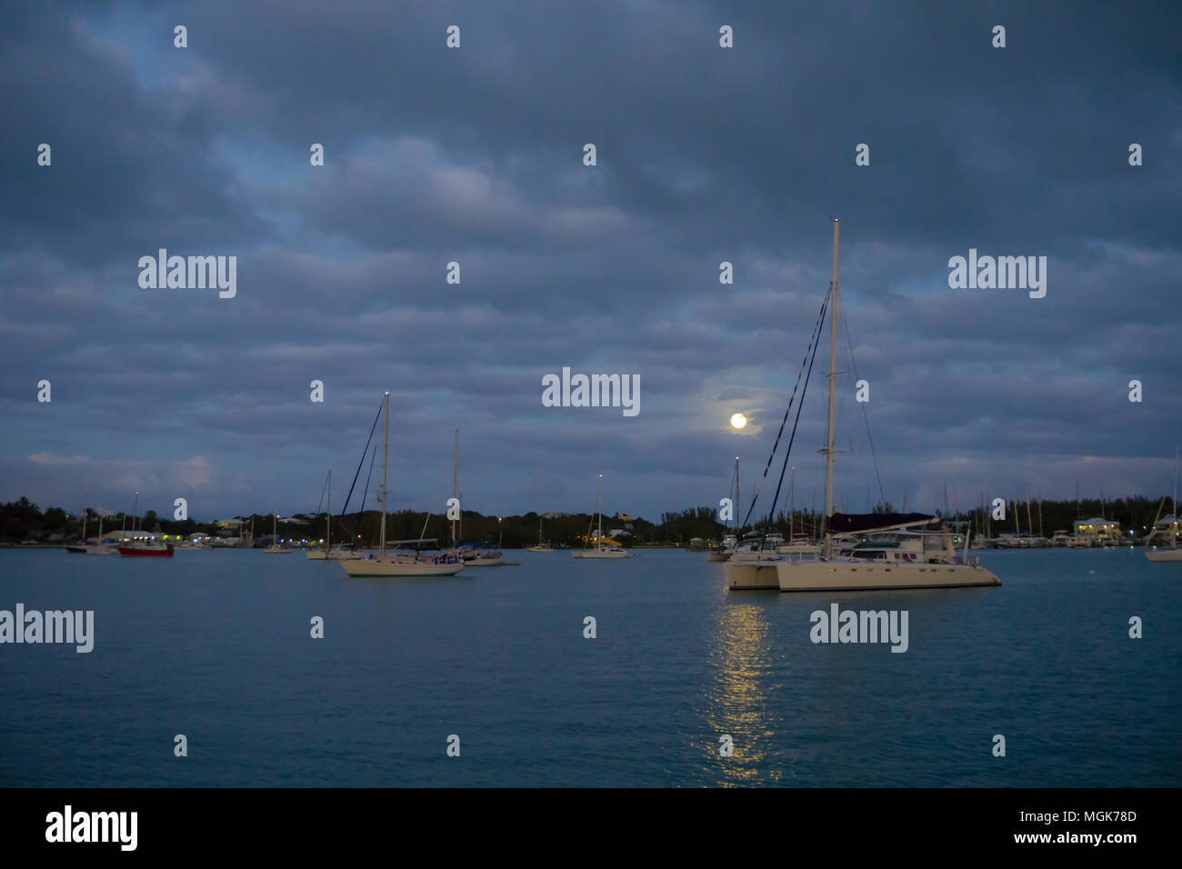 Der Mond Peaks durch Lila Wolken an einem dunklen Abend, scheint ein ruhiger Hafen voller Segelboote und Katamarane Chartern Stockfoto