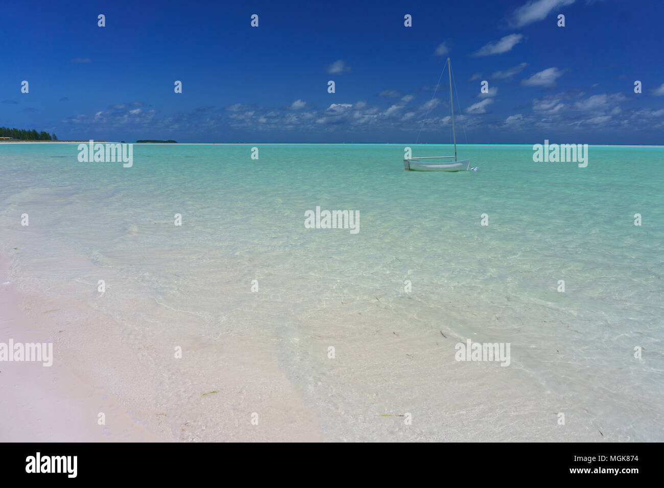 Spanish Wells, Eleuthera, Bahamas helle weiße Sandstrand und das klare grüne und blaue Wasser mit einem klassischen kleinen Segelboot offshore verankert Stockfoto