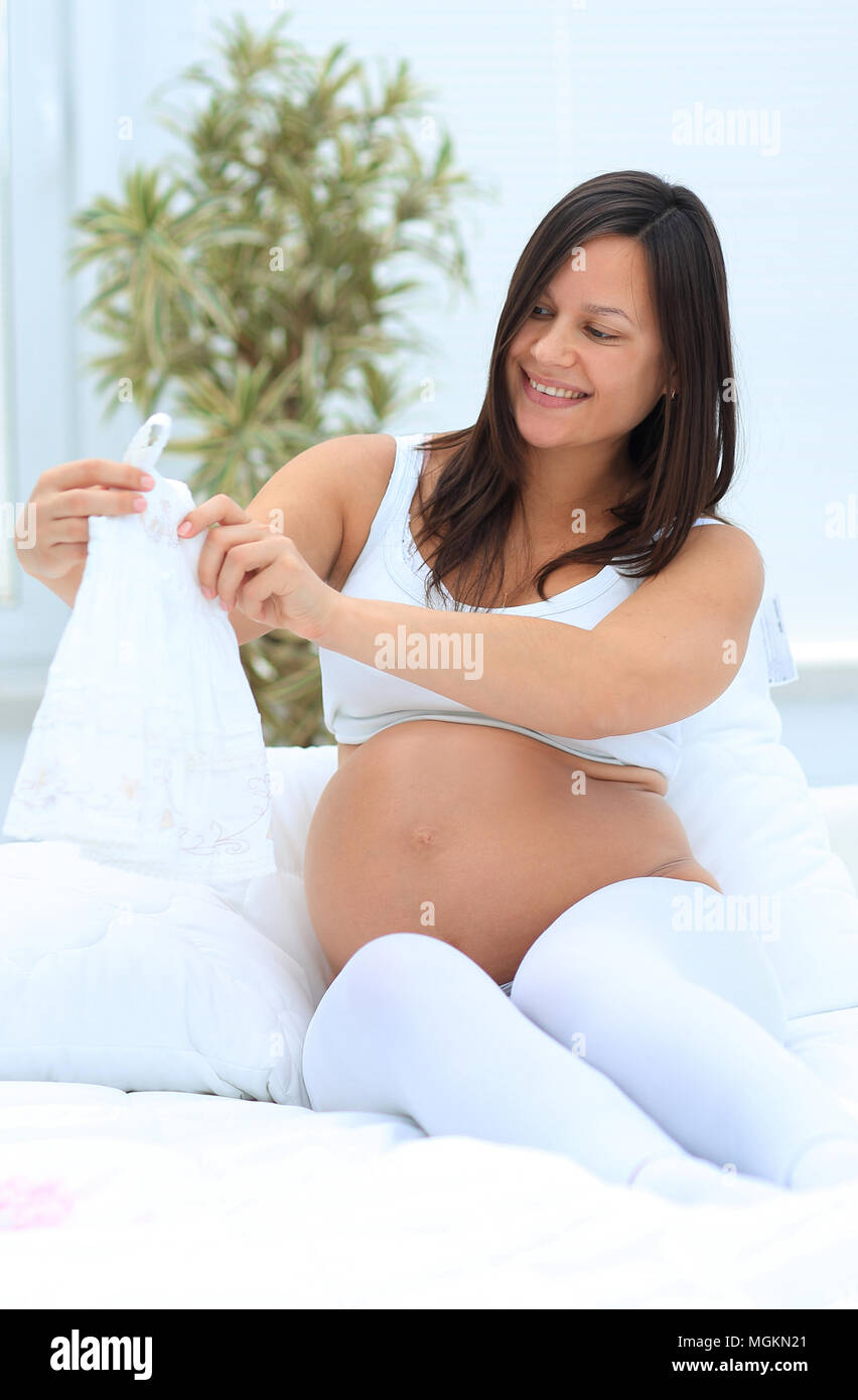 Schwangere Frau angesichts der Kinder T-Shirt, auf dem Bett zu sitzen. Stockfoto