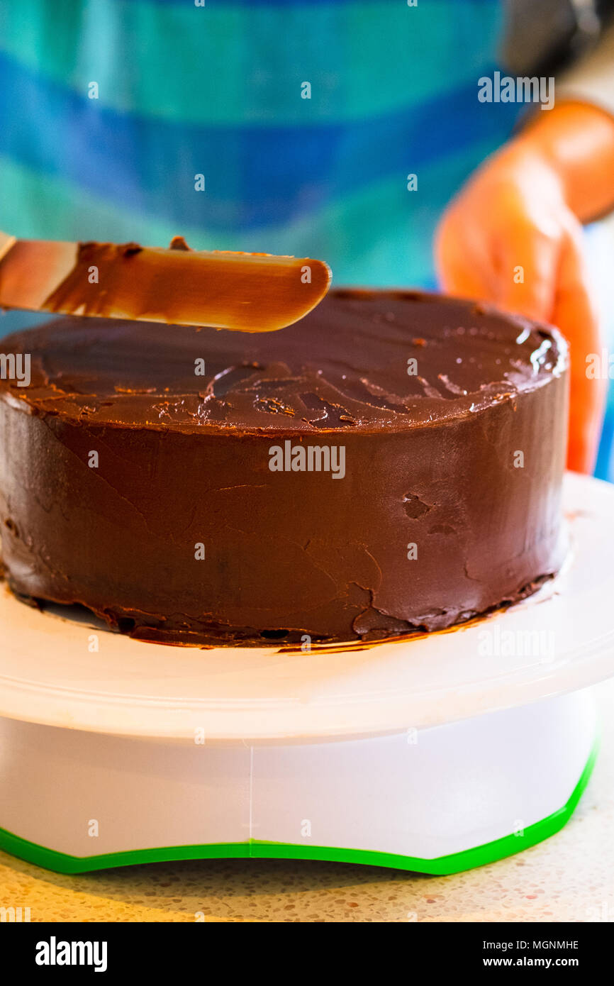 Eine Frau, die Ganache Vereisung oder Zuckerguss um einen Kuchen, mit einem Spatel Stockfoto