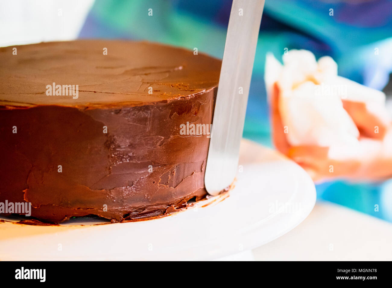 Eine Frau, die Ganache Vereisung oder Zuckerguss um einen Kuchen, mit einem Spatel Stockfoto