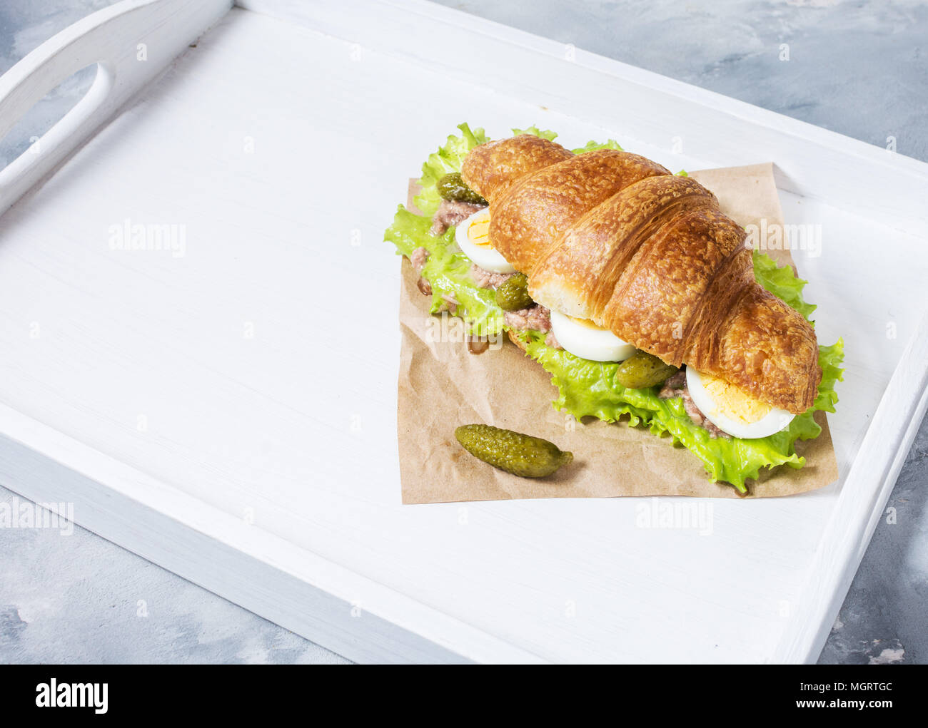 Croissant Sandwich mit Thunfisch, hart gekochte Eier, Salat und Gurke auf weißen Fach Frühstück Konzept. Platz kopieren Stockfoto