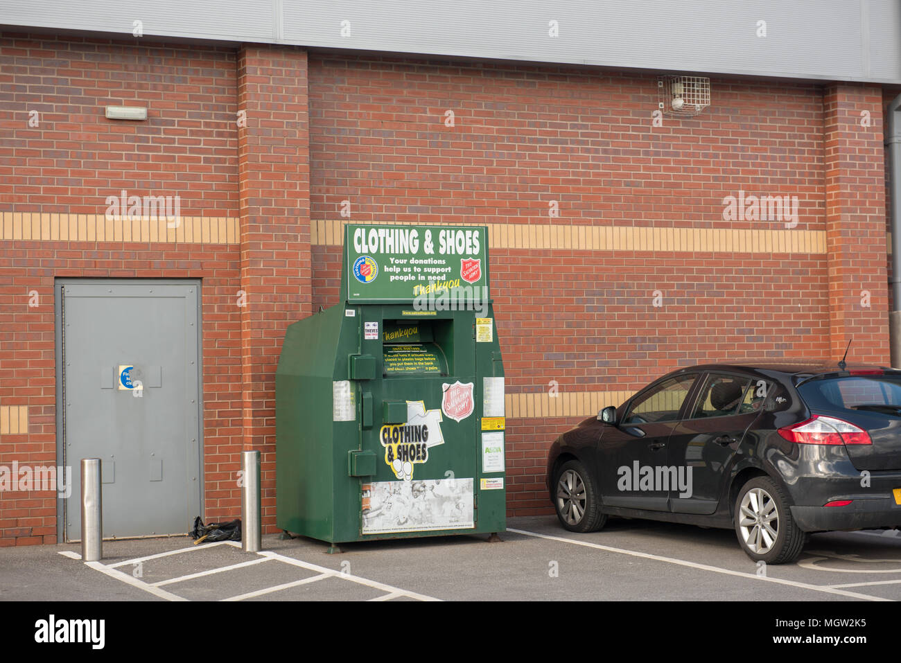 Ein Spendenbehälter für Kleidung und Schuhe neben einem geparkten Auto vor einem Backsteingebäude in Großbritannien Stockfoto