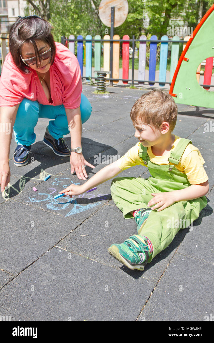 Mama und cute Boy zeichnen Alphabet mit bunter Kreide auf Asphalt. Sommer Aktivität und kreative Spiele für kleine Kinder. Zeit mit der Familie. Happy Mother's Day. Stockfoto