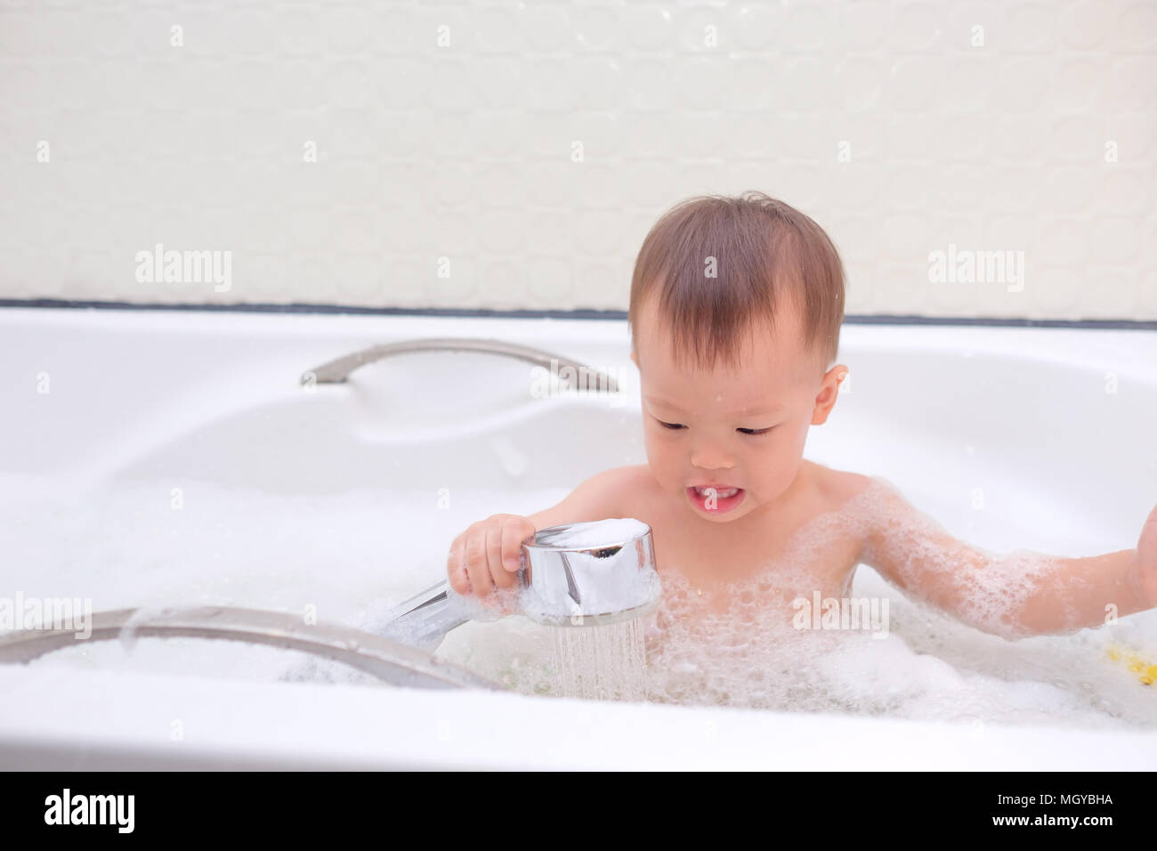 Süße kleine Asiatische 18 Monate / 1 Jahr altes Kleinkind Baby Junge Kind  Spaß sitzen in der Badewanne, eine Dusche, in der Hand eine Dusche nehmen,  indem er sich i Stockfotografie - Alamy