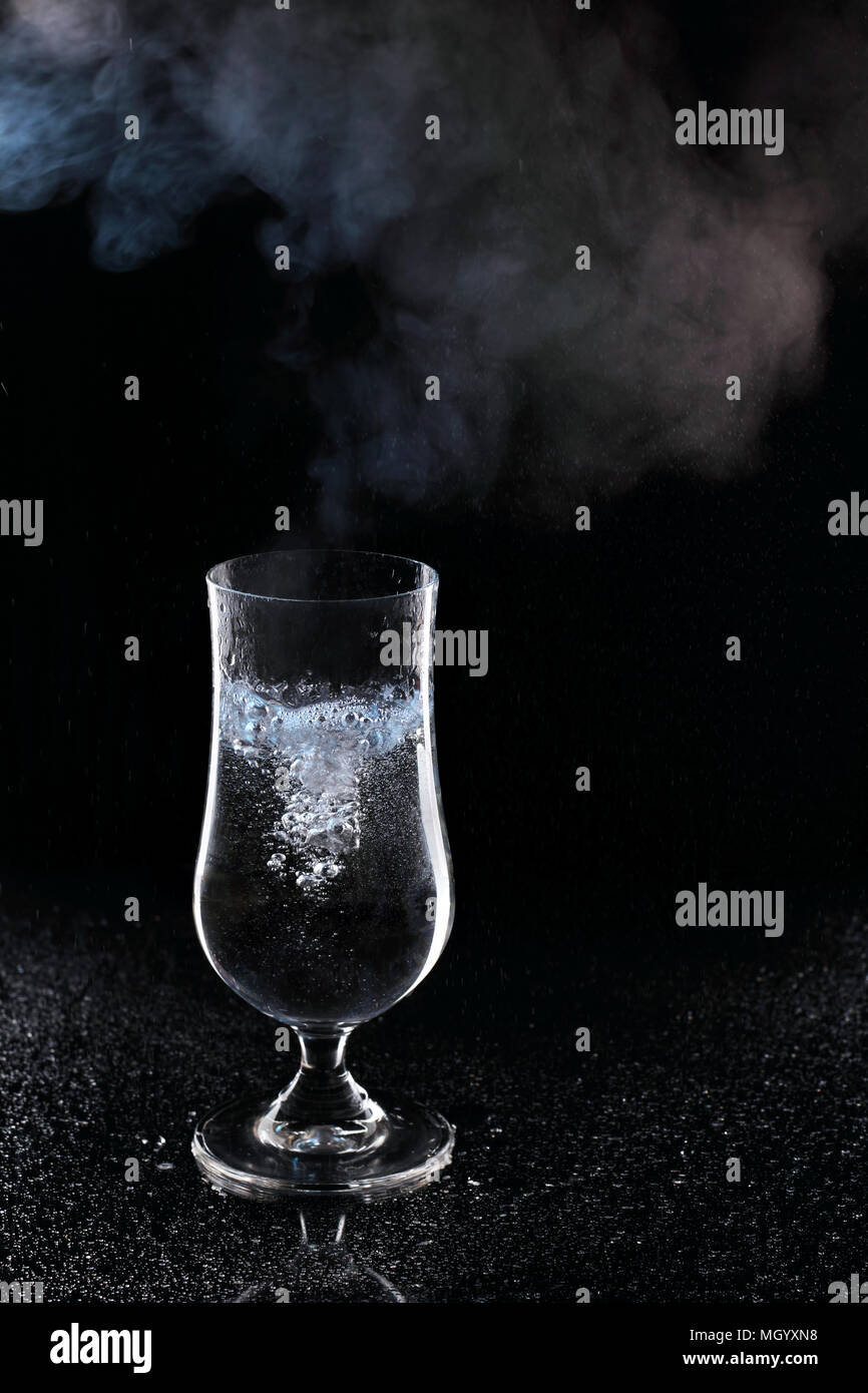 Kochendes Wasser in ein Glas mit Dampf über einem Glas auf schwarzem Hintergrund Stockfoto