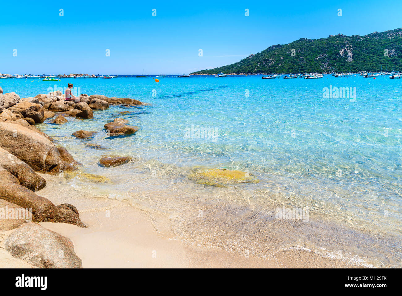 Strand von Santa Giulia, Insel Korsika - May 22, 2015: Junge Frau sitzt auf Felsen an einem wunderschönen Strand mit kristallklarem Wasser. Diese französische Insel ist pop Stockfoto