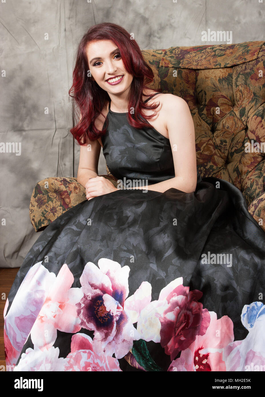 Hübsche junge Rothaarige in Schwarz prom Kleid auf floralen Muster Stuhl Stockfoto