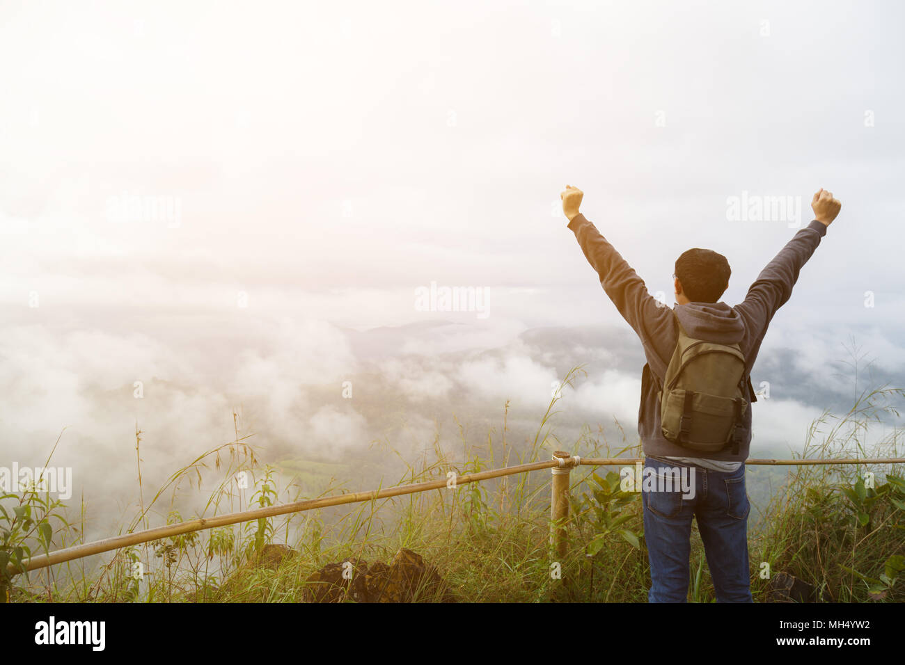 Im mittleren Alter asiatischer Mann Rucksack entspannen und auf die Berge im Hintergrund aktualisieren" ist eine Landschaft mit hohen Bergen, weiße Wolken und Nebel. Stockfoto