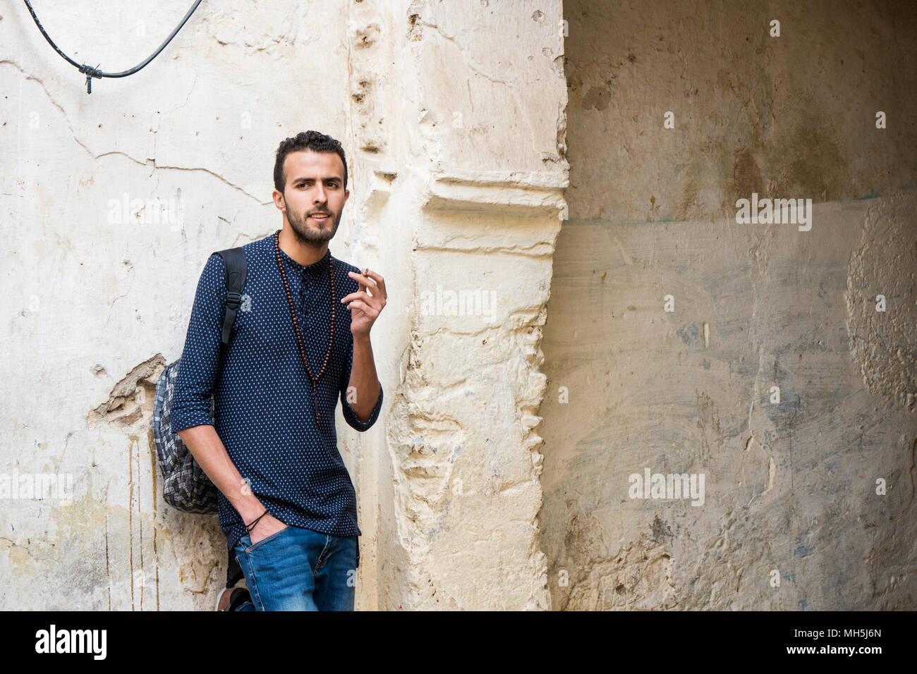 Junge muslimische Mann Rauchen einer Zigarette in Freizeitkleidung stehend durch die zerstörte Wand Stockfoto