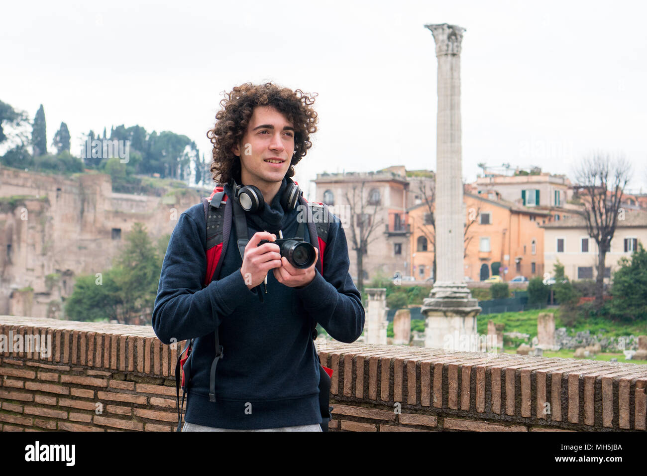 Hübscher junger Tourist mit lockigem Haar Fotos von Forum Romanum in Rom, Italien. Junger Mann mit seiner Kamera Stockfoto