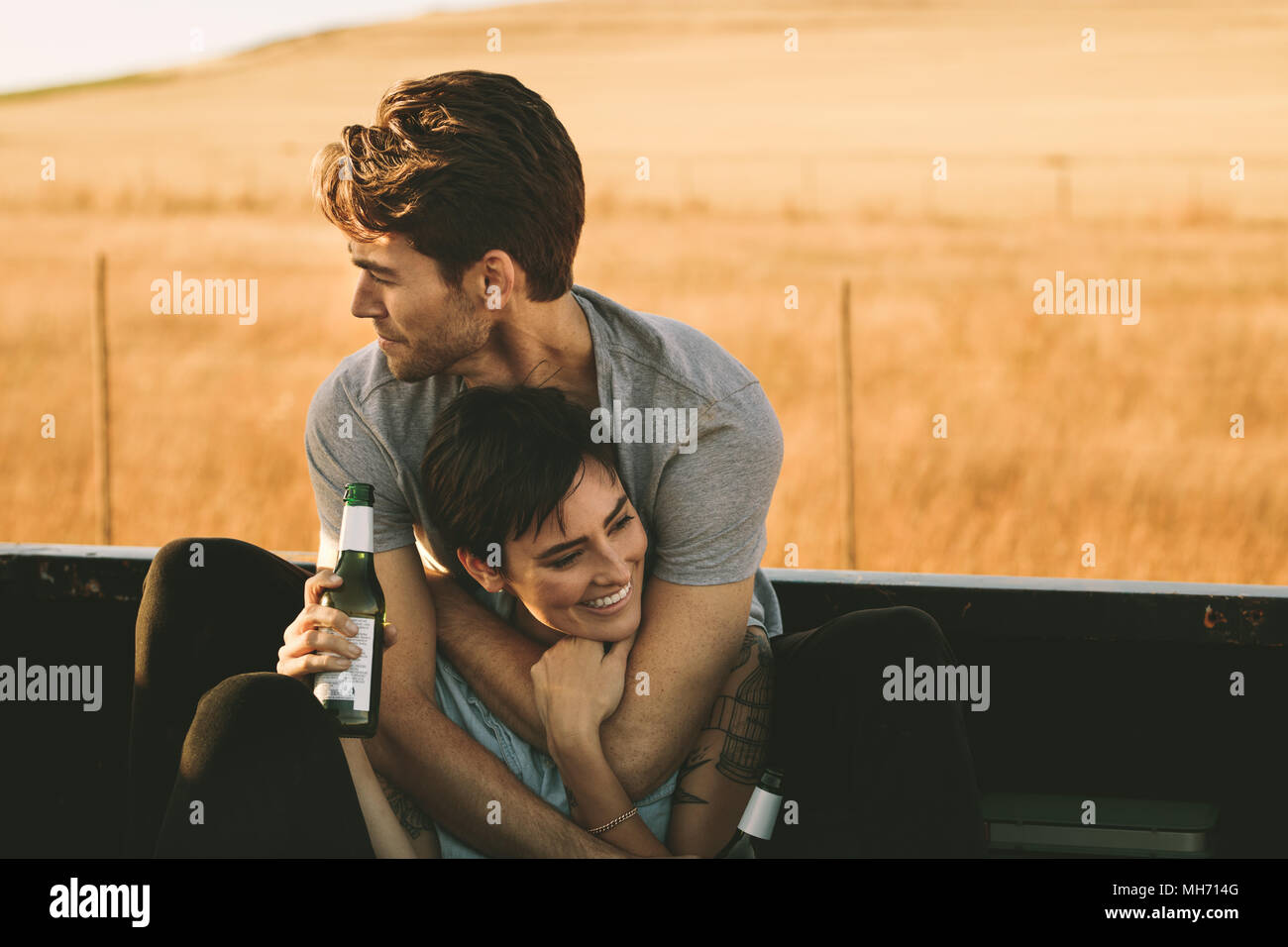 Paar in der Rückseite ihres Pickup Truck sitzen, genießen die Straße Reise im Land. Mann und Frau, die einander und geniessen Sie eine Flasche Abakus Stockfoto