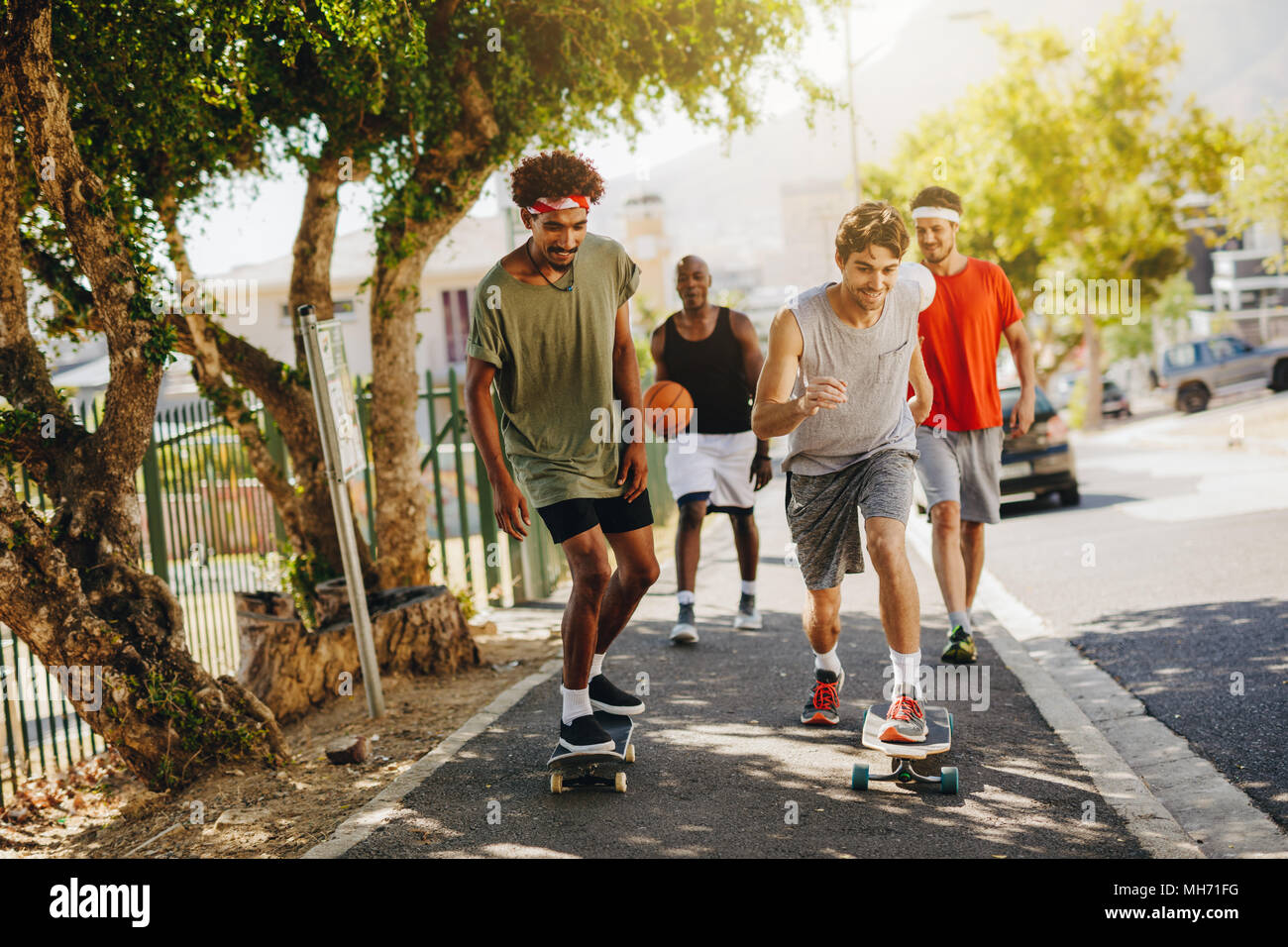 Zwei Männer Schlittschuhlaufen auf Skateboard auf einem Gehsteig, während ihre Gehilfen feuern Sie. Basketball Jungs gehen auf Asphalt mit skateboards. Stockfoto