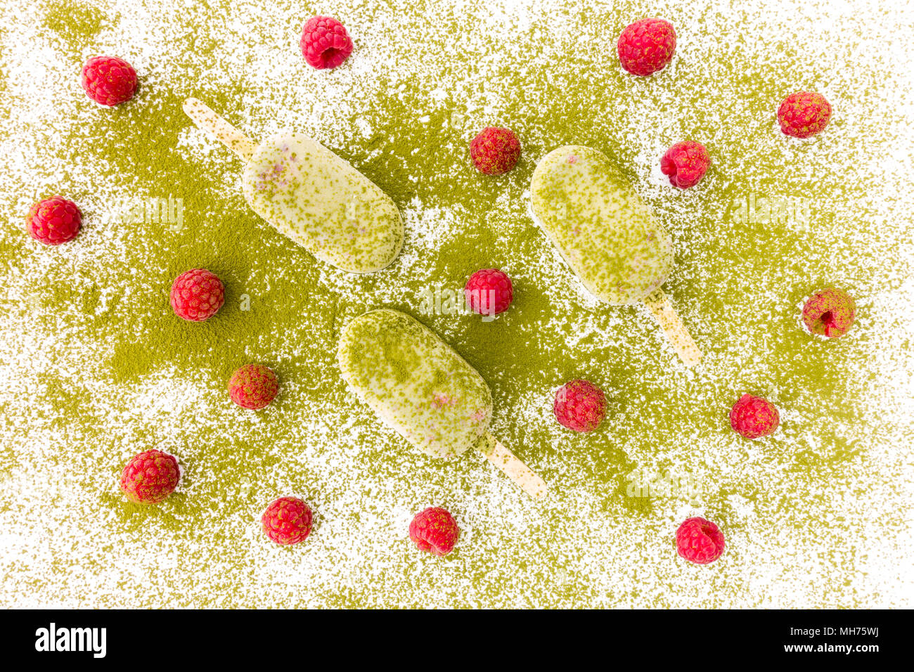 Frische Himbeeren und drei Matcha und Himbeere Eis am Stiel auf weißem Hintergrund bestäubt mit Matcha Pulver. Stockfoto