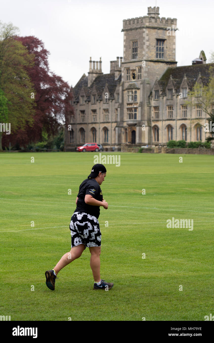 Ein Läufer in Cirencester parkrun mit der Königlichen Universität für Landwirtschaft in der Ferne, Gloucestershire, VEREINIGTES KÖNIGREICH Stockfoto