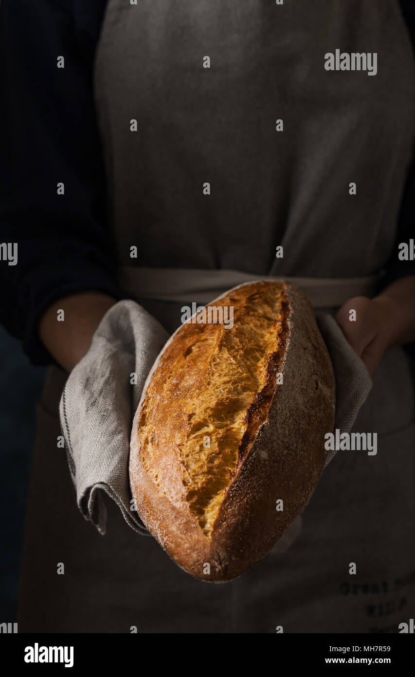 Die Frau Hände mit frischen, hausgemachten Brot. Zusammensetzung in dunklen Farben Stockfoto