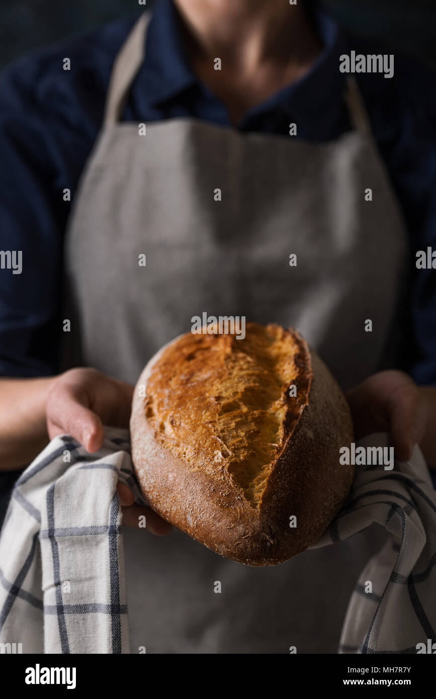 Baker Holding frisches hausgemachtes Brot. Zusammensetzung in dunklen Farben Stockfoto
