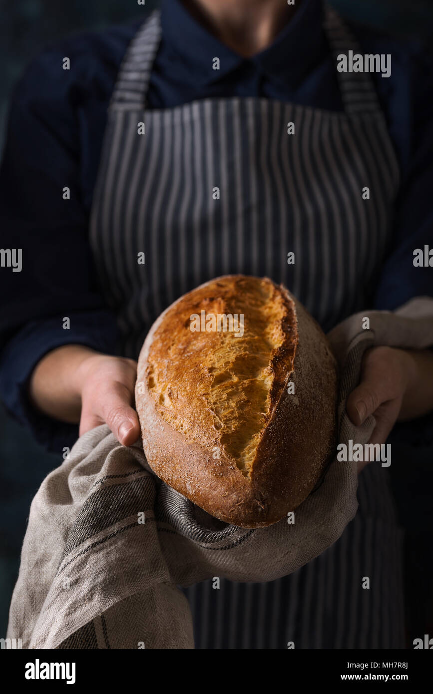 Baker Holding frisches hausgemachtes Brot. Zusammensetzung in dunklen Farben Stockfoto