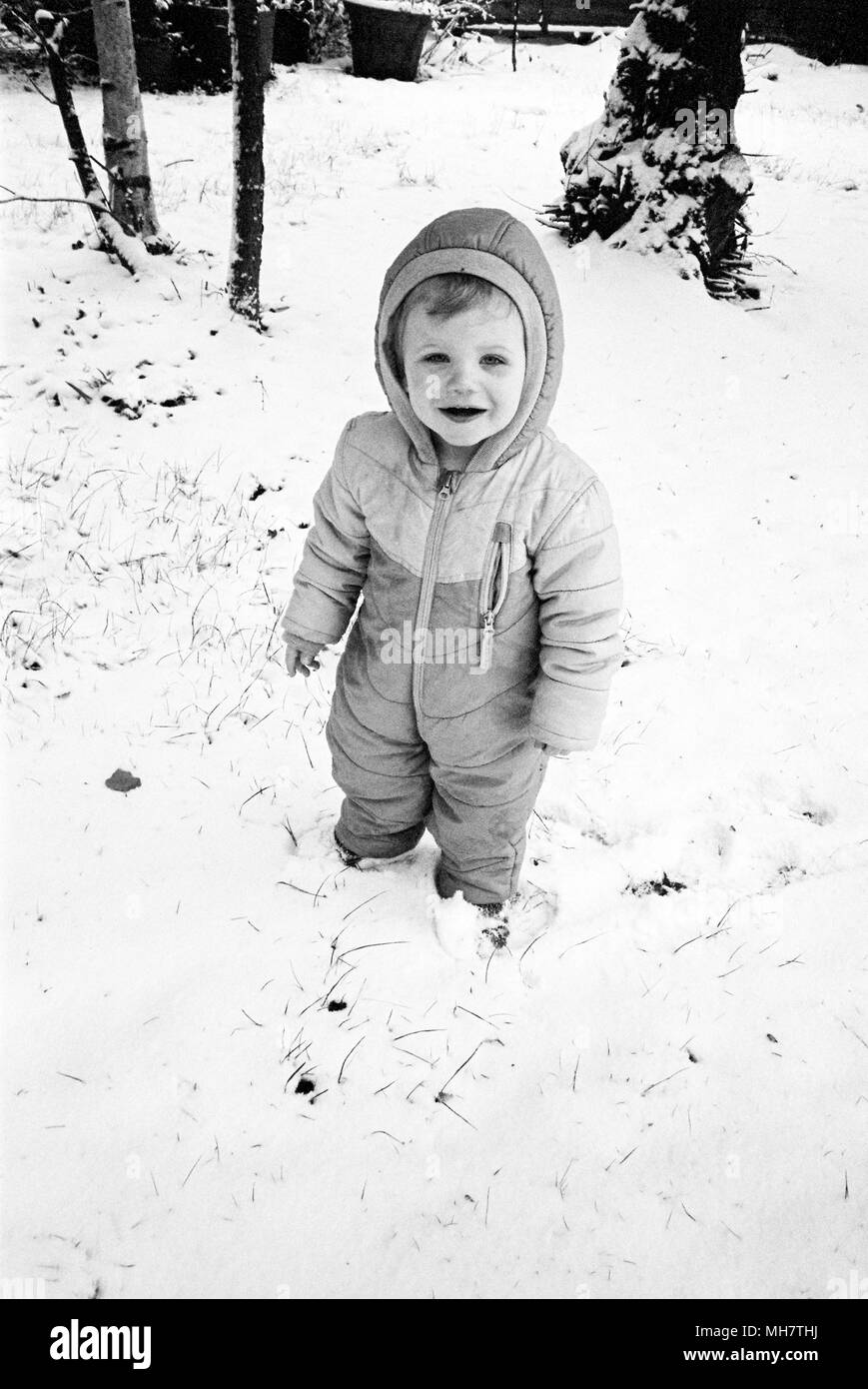 Achtzehn Monate alten Baby boy in ein schneeanzug, Medstead, Alton, Hampshire, Vereinigtes Königreich. Stockfoto