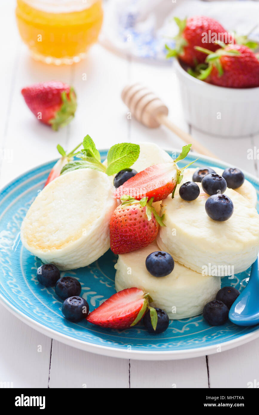 Mini Käsekuchen mit Früchten auf einem blauen Schild. Kalten Sommer Dessert oder Snack. Gesunde Cottage Käse Käsekuchen mit Beeren und Früchte Stockfoto