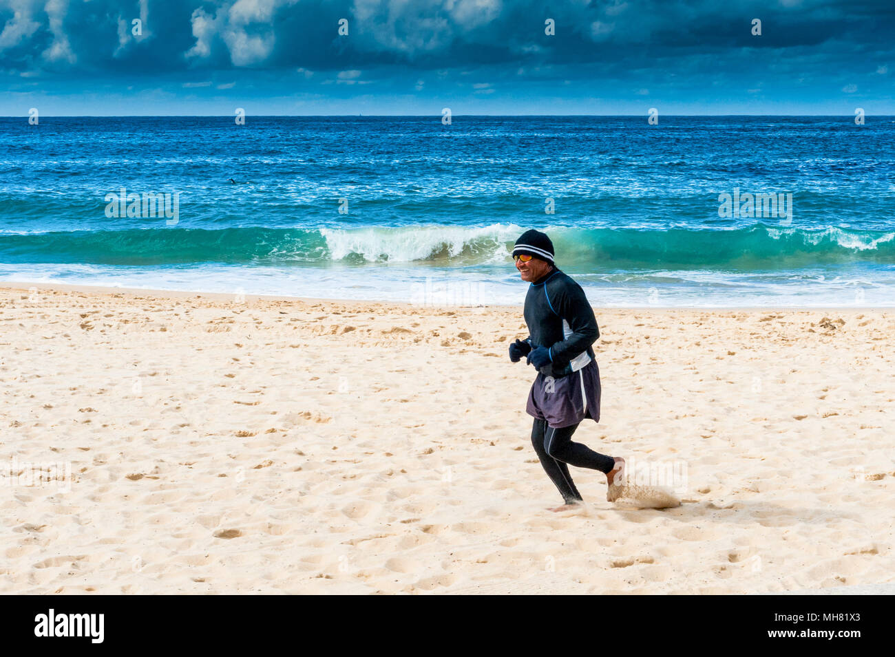 Ein Jogger macht sich auf den Weg entlang der berühmten Bondi Beach, Sydney, Australien, mit einer stürmischen bewölkten Himmel im Hintergrund. Stockfoto