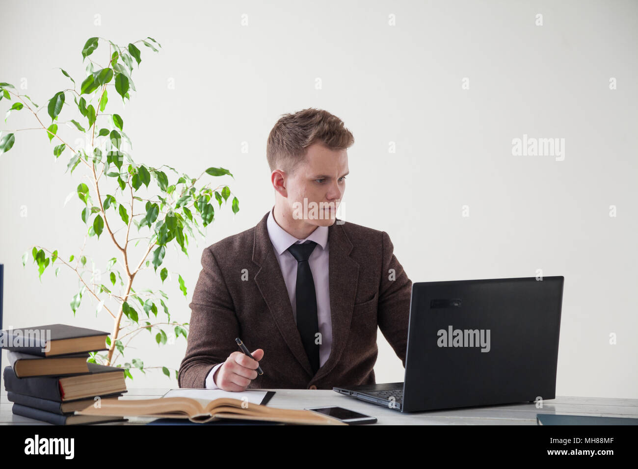 Ein Mann im Anzug arbeitet an einem Schreibtisch mit Computer und Bücher im Büro Stockfoto